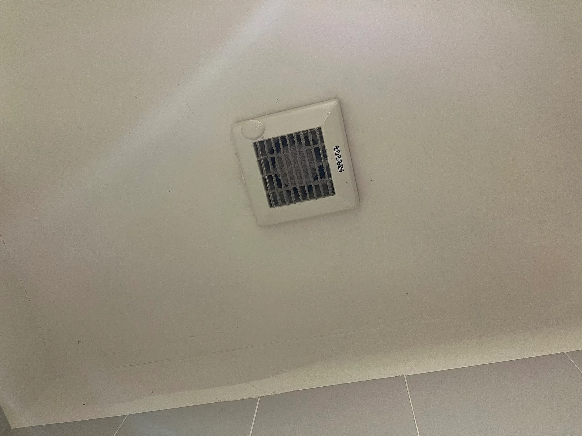 Grille d'extraction d'air carrée et blanche au plafond d'une salle de bain carrelée