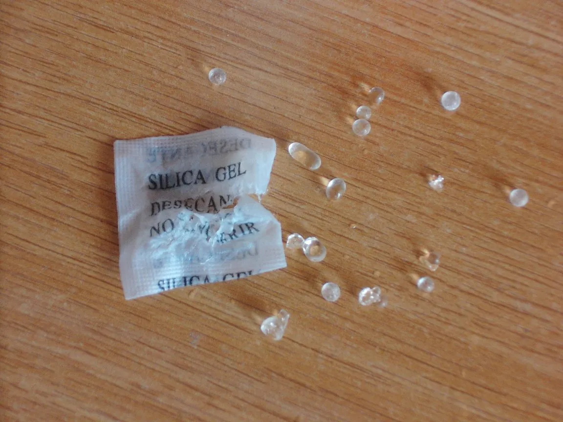 Petit sachet de gel de silice ouvert, ses billes transparentes répandues sur une table en bois